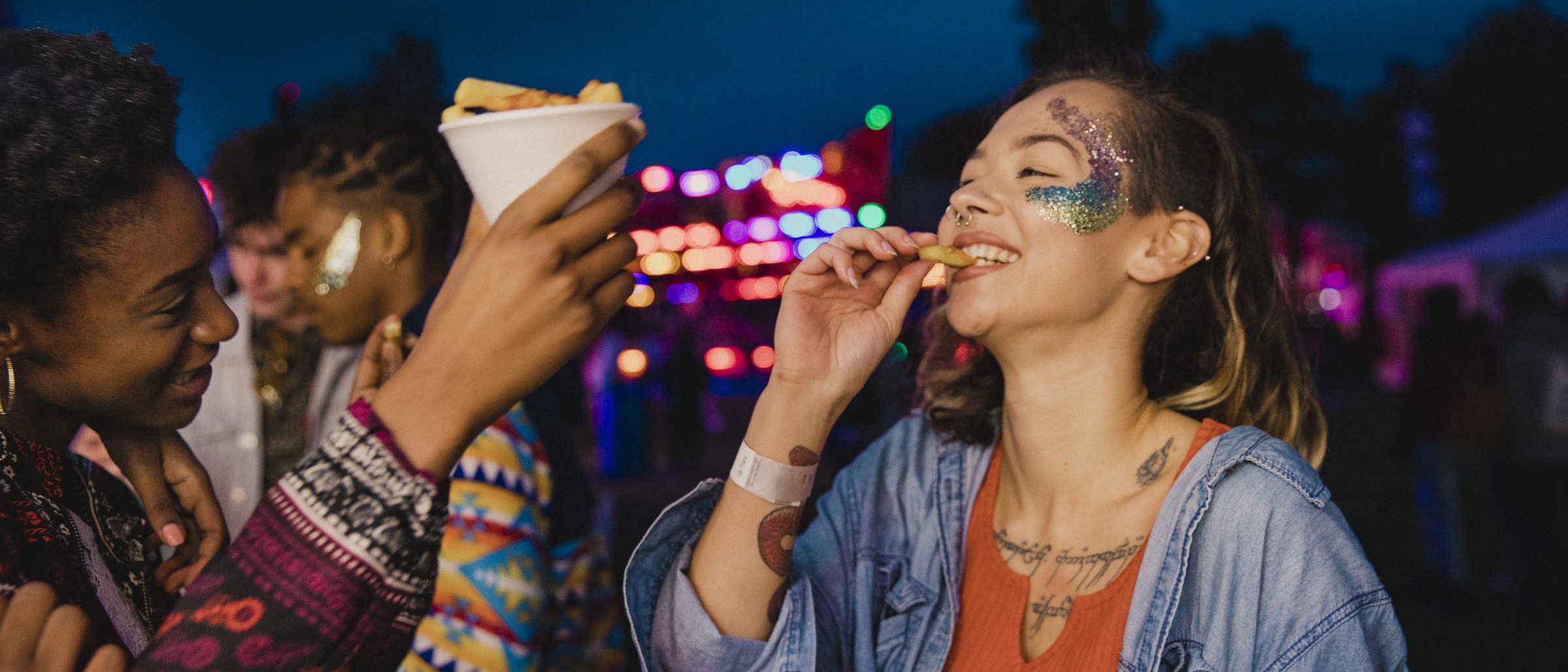 Junge Menschen abends auf einem Festival, im Hintergrund bunte Lichter